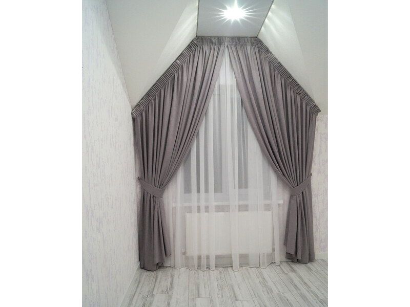 Серые шторы с белым тюлем в мансардной комнате с треугольным окном.